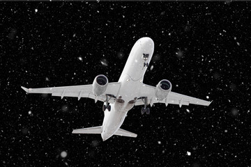 white passenger plane has released its landing gear and is landing through falling snow against background of dark night in winter