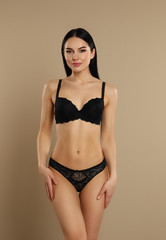 Fototapeta premium Beautiful young woman in black underwear on beige background