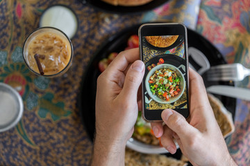 Photo of food on a smartphone. Hands of a man holding a phone with a photo on the screen, food photo, blogger, social networks.