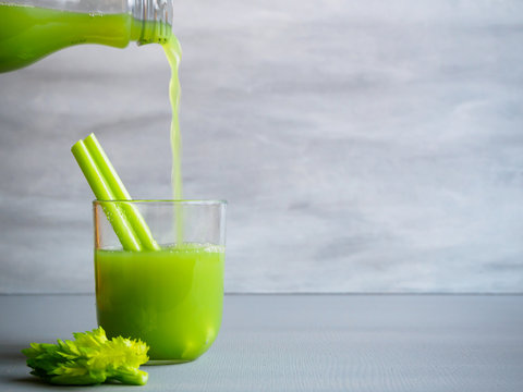 Flasche mit gr&uuml;nen Selleriesaft flie&szlig;t in ein Trinkglas afu einem grauen Hintergrund, Naturkost, gesunde Ern&auml;hrung