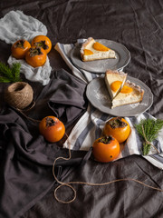 persimmon cheesecake on a dark background. Pieces of cake decorated with persimmons and Christmas tree branches.