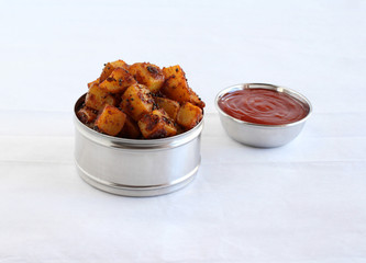 Crispy potato fry, or aloo fry, an Indian vegetarian snack and a side dish for items like chapati, in a steel box, and ketchup in a bowl.