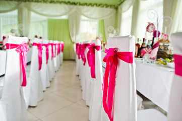 Beautiful wedding set decoration in the restaurant. Pink ribbons on chairs.
