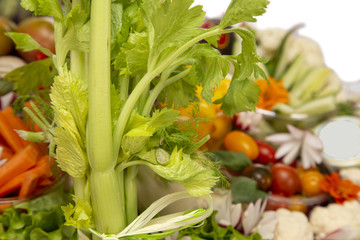 Stick of celery in a gift basket with a selection of mixed vegetables on a white background