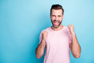 Fototapeta premium Photo of attractive guy ecstatic emotions win lottery money prize yelling loud rejoicing raise fists wear casual pink t-shirt isolated blue color background