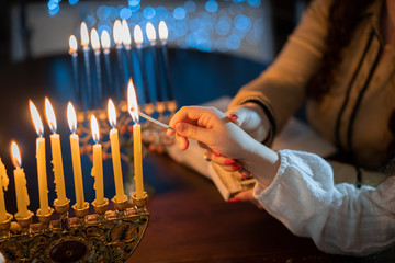 jewish holiday Chanukah/Hanukkah family selebration. Jewish festival of lights. Children lighting candles on traditional menorah over glitter shiny background - obrazy, fototapety, plakaty