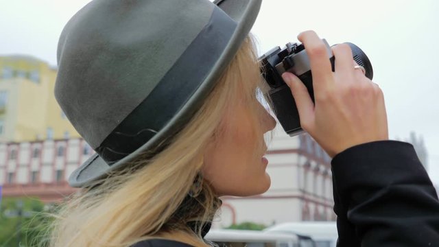A young Caucasian woman, a hipster in a hat takes photos on an old vintage film camera. Concept journalist blogger for print edition in work.