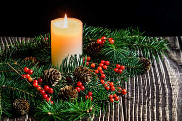 Christmas tree, red berries and burning white candles on a wooden table