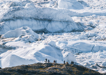 People sitting standing in front of huge glacier wall of ice. Icefjord Ilulissat. Jakobshaven Eqip...