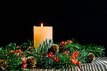 Christmas tree, red berries and burning white candles on a wooden table