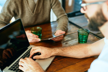 Attractive bearded man with glasses in a cafe working on laptop and chatting with a friend	