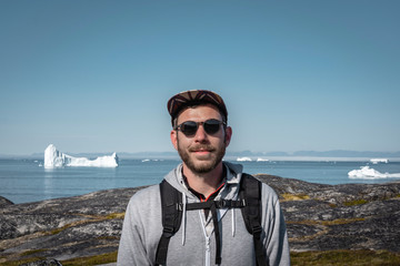 Young traveler tourist sitting standing in front of huge glacier wall of ice. Icefjord Ilulissat....