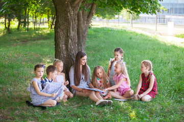 children hold a lesson with the teacher in the park on a green lawn.