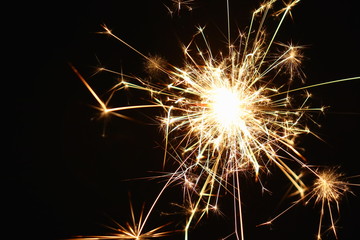 Christmas and New Year's illumination. Burning sparklers scatter bright exploding strips of sparks on a dark background.