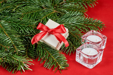 Fototapeta na wymiar New Year's composition, Christmas decorations. Gift box in white packaging with a red bow next to spruce branch and glass China candles on a red velvet background. With copy-space