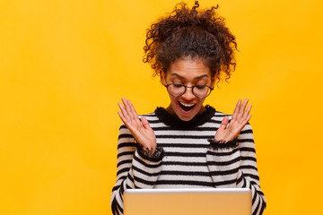 Young african american woman working using computer laptop afraid and shocked with surprise expression, fear and excited face in studio at yellow background.Close up