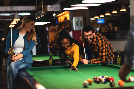 Four smiling friends in bar playing billiard together.