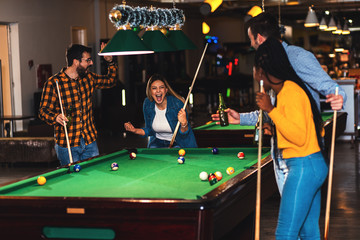 Four smiling friends in bar playing billiard together.