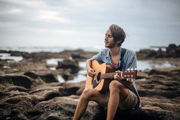 Romantic young man with a guitar on the beach