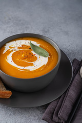 Pumpkin soup with cream on grey stone background. Copy space.