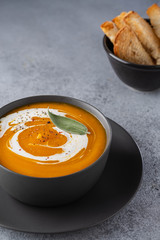 Pumpkin soup with cream on grey stone background. Copy space.