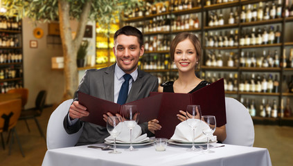 leisure and luxury concept - smiling couple with menus over restaurant or wine bar background