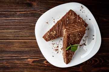 Slice of chocolate cake with milk filling and raspberry on white plate on dark wooden background.