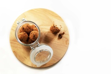 Energy balls in a glass jar. The dishes are on a wooden stand on a white background. Sweet snack in cocoa powder. Healthy snack, healthy food. Food without harm. Copy space, top view and isolated