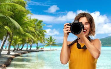 travel, tourism and photography concept - happy woman photographer in yellow top with digital camera on vacation over tropical beach background in french polynesia