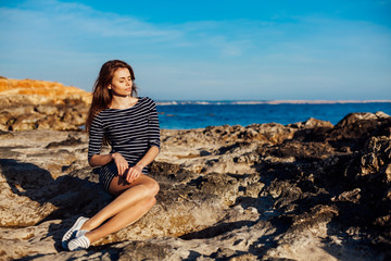 Fototapeta na wymiar girl sits on the rocky beach enjoys sunshine