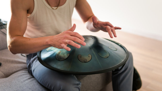 Close up of man hands playing hang drum indoors. Unusual music instrument.