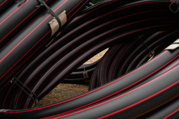 Black rubber or plastic pipes with a red lines as a construction material and equipment at building site. Using as a water pipe.