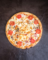 Pizza with mushrooms, tomatoes, smoked sausage and cheese on a dark background