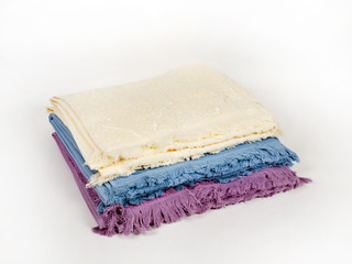 Three towels of different colors with a fringe are stacked in a stack on a light background, side view