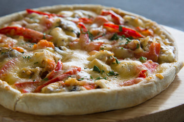 Hot pizza with tomatoes and pepper on a wooden plate.