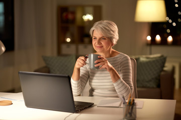 technology, old age and people concept - happy senior woman with laptop drinking coffee at home in...