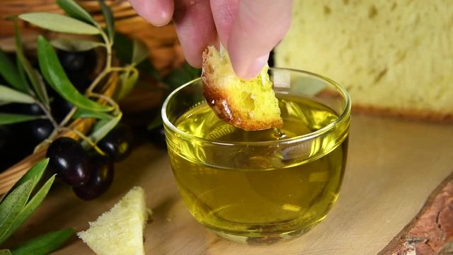 A hand dips bread into a natural Italian organic golden cold pressed olive oil in a transparent bowl. Slow motion. The concept of nature and healthy food, healthy and natural. Bio Olives and Puglia 