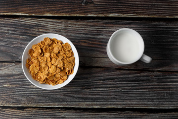 White plate with healthy cereal breakfast and cup of milk on a wooden surface. Top view.