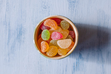 Bowl of jelly sugary candies on white wooden background. 
