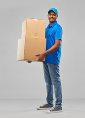 mail service and shipment concept - happy indian delivery man with parcel boxes in blue uniform...