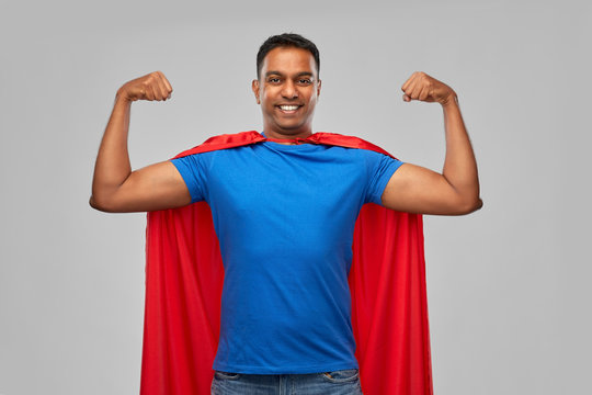 super power and people concept - indian man in red superhero cape showing his muscles over grey background