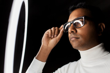 future technology, augmented reality and vision concept - indian man in glasses under white illumination over black background