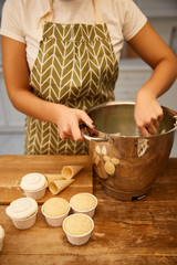 Cropped view of confectioner making cream beside cupcakes and waffle cones on wooden table