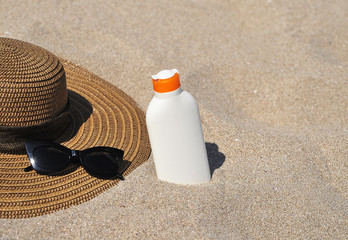 Hat, sunglasses and sun protection cream on sand background.