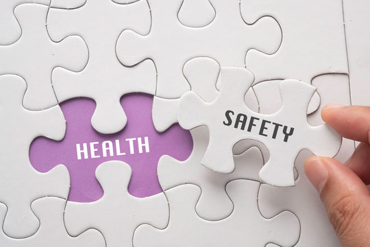 Hand hold piece of puzzle written SAFETY revealing word HEALTH. Health and Safety concept.