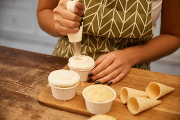 Cropped view of confectioner adding tasty cream on baked cupcakes