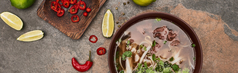 top view of pho in bowl near lime, chili on stone background, panoramic shot