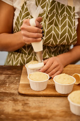 Cropped view of confectioner decorating cupcakes with pastry bag