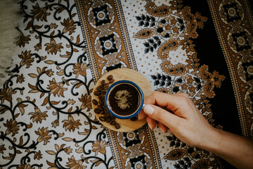 Top view of woman's hand holding espresso cup on floral pattern