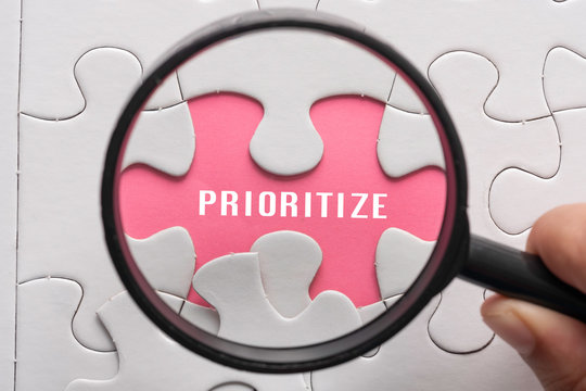 Hand hold magnifying glass with puzzle, focus on the word Prioritize. Business concept.